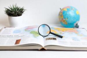 Magnifying glass on open book displaying world map with globe in background. Ideal for themes of global research, travel, geography, exploration, and education visuals photo