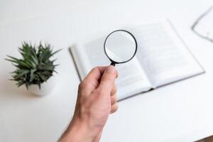 Hand holding magnifying glass over open book, symbolizing keyword search, SEO optimization, and in-depth content analysis, representing focused exploration for digital marketing and research photo