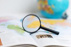Magnifying glass on atlas with globe in background, symbolizing geography studies, school learning, global exploration, and gaining knowledge about world maps and travel photo