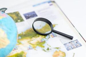 Magnifying glass on world atlas with globe nearby, symbolizing global exploration, travel planning, geographic research, and a deeper understanding of international locations and destinations photo
