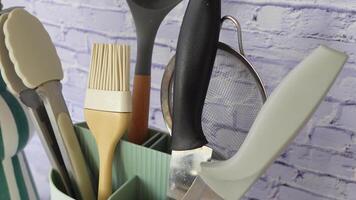 A variety of assorted kitchen tools neatly arranged in a modern holder against a rustic brick wall video
