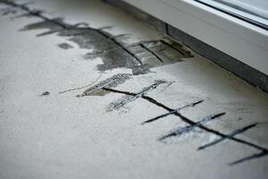 Repairing cracks in concrete floor near window using sealant. Renovation process in house under construction photo