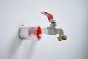 Close-up of water faucet with red handle protruding from white wall in empty apartment. Plumbing work during home renovation photo