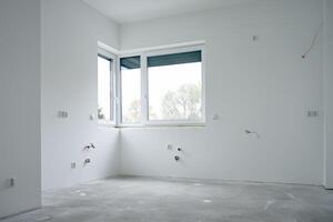 Spacious empty apartment undergoing renovation with large window, concrete floor and white walls. New building under construction photo