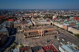 Aerial view of Krakow main market square with historic Cloth Hall , Sukiennice surrounding colorful buildings on sunny day. Cityscape of Krakow in Poland with tourists walking in old town photo