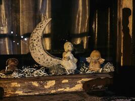 A cozy window display shows delicate figurines of angels and a crescent moon, surrounded by shredded paper for a soft, whimsical touch. The warm glow of light enhances the nostalgic and serene atmosph photo