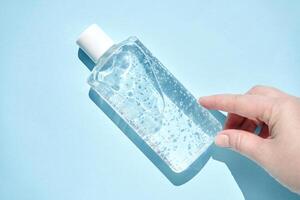 Hand reaching for clear sanitizer bottle with bubbles on blue background for hygiene and cleanliness concepts. photo