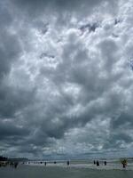 A cloudy sky over the ocean with people walking on the beach photo