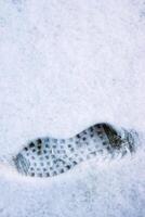 Closeup of a single black footprint in a white snow left by a boot, symbolizing color and texture contrast and outdoor adventure on a cold winter day. Copy space photo