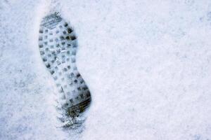 Closeup of a single black footprint in a white snow left by a boot, symbolizing color and texture contrast and outdoor adventure on a cold winter day. Copy space photo