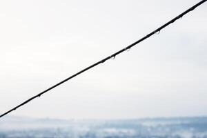 Minimalistic closeup of vineyard wire with delicate water droplets against cloudy overcast sky. Rain drops against a blurred horizon. Copy space photo