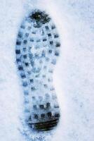Closeup of a single black footprint in a white snow left by a boot, symbolizing color and texture contrast and outdoor adventure on a cold winter day. Copy space photo