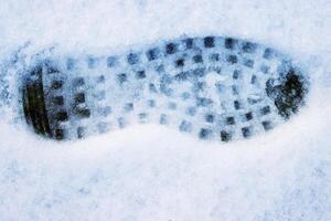 Closeup of a single black footprint in a white snow left by a boot, symbolizing color and texture contrast and outdoor adventure on a cold winter day. Copy space photo
