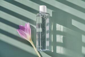 Bottle of facial toner or cleanser on a green background with stripes shadows. photo