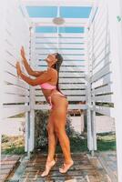 A woman in a bikini stands in front of a white shower stall. She is smiling and she is enjoying the moment photo