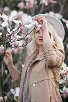 Magnolia flowers woman. A blonde woman wearing a white hat stands in front of a tree with pink flowers. She has a smile on her face and she is enjoying the beautiful scenery. photo