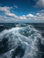 Waves churn in the ocean under a cloudy blue sky in the afternoon photo