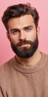 Young man with a beard posing against a pink background in casual sweater photo