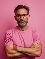 A sad man with glasses crossing his arms against a pink backdrop photo