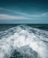Waves crash behind a boat on a clear ocean day near the horizon photo