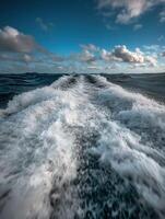 Waves churn in the ocean under a bright blue sky with clouds photo
