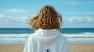 Person with wavy hair standing on sandy beach facing the ocean photo