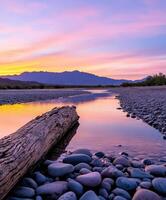 Sunset over a tranquil river with pebbles and mountains in view photo