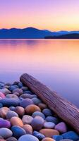 Sunset over calm waters with colorful pebbles and a driftwood log photo