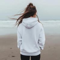 Young woman in white hoodie stands by the beach on a cloudy day photo