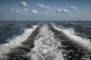 Wake trails from a boat moving across calm water under a cloudy sky photo