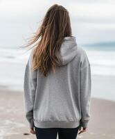 Young woman in gray hoodie stands on beach with wind in hair photo