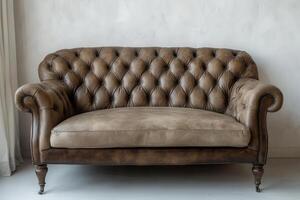 Elegant brown leather tufted sofa placed against a neutral wall photo
