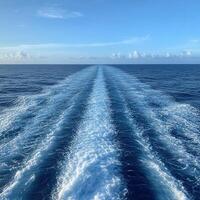 Wake trails behind a boat on a calm ocean under a clear sky photo