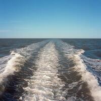 Waves trailing behind a boat on a calm ocean under clear blue sky photo