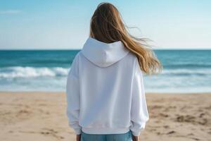 Woman wearing a white hoodie stands on sandy beach by the ocean photo