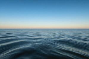 Calm ocean waves under a clear sky at sunset near a tranquil coastline photo