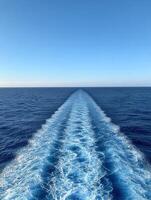Gentle ocean waves trail behind a boat under clear blue sky photo