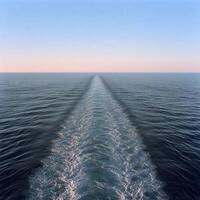 A tranquil ocean view showing wake trails from a boat during sunset photo