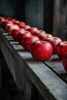 Fresh red apples lined up on a wooden shelf in a rustic setting photo
