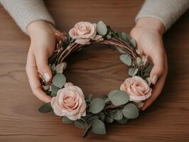 Person holding a floral crown with pink roses and greenery on a table photo