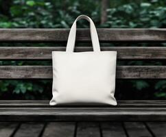 A simple white tote bag rests on a wooden bench in a green park photo