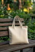 A simple beige tote bag rests on a wooden park bench surrounded by greenery photo