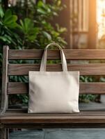 A simple beige tote bag rests on a wooden bench in a sunny garden photo