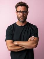 A sad man stands with crossed arms in front of a pink backdrop photo