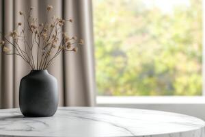 A simple black vase with dried flowers on a marble table by a window photo