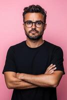 A sad man with glasses stands with crossed arms against a pink background photo
