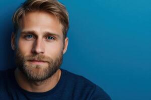 Young man with a beard and blue eyes posing against a blue wall photo