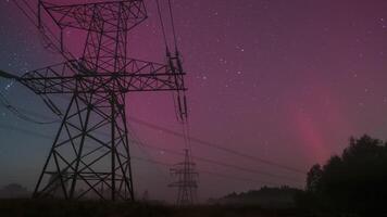 Intensifying northern lights create a stunning display over power lines, showcasing vibrant shades of pink, purple, and red against a dark, starry sky in a remote countryside setting. Time lapse video