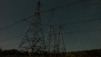 Nighttime view of high voltage power lines against the backdrop of moving stars in the night sky on a moonlit night. Concept of electricity and energy generation. Time lapse video