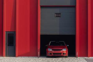 A red car is parked at the exit of a red garage photo